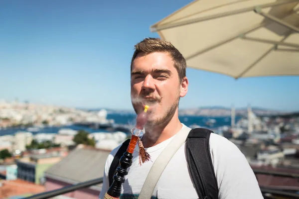 Un joven sonriente con bigote fuma una cachimba en la terraza — Foto de Stock
