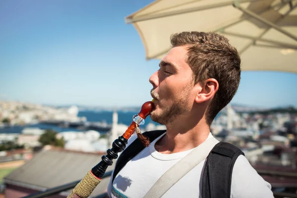 Un joven guapo con barba fuma una cachimba en la terraza. — Foto de Stock