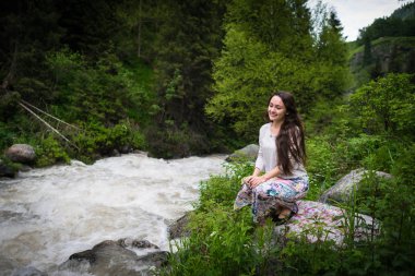 Genç kadın Milli Parkı taş oturur ve dağ nehir kaynama görünüyor