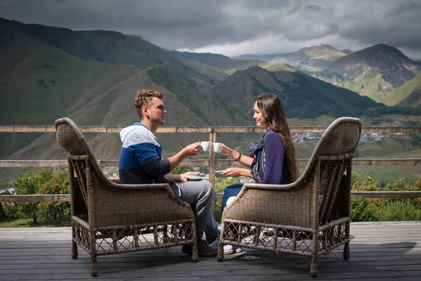 Jovem casal de bom humor senta-se no terraço com xícaras de café pela manhã — Fotografia de Stock
