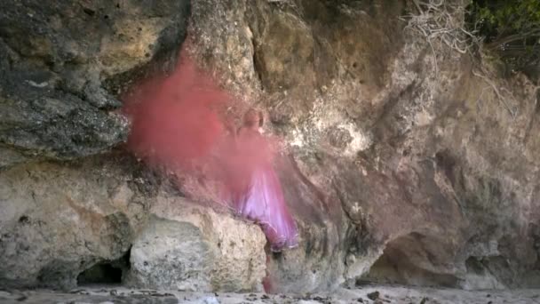 穿着粉色蓬松连衣裙的年轻悠闲女子站在石头上 背靠着巨大的岩石和浓烟摆姿势 — 图库视频影像