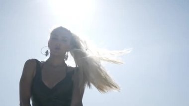 Sarışın ve makyajlı çekici bir kadın. Siyah mayo giymiş. Sahilde dans ediyor ve açık gökyüzü ile poz veriyor..