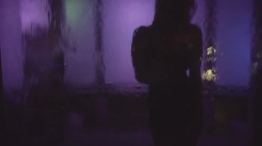 Siyah, küçük elbiseli, sarı saçlı genç bir kadının silueti. Dans eden ve sanat objesinde poz veren kız Düşen suyla ve renk değiştiren ışıkla.