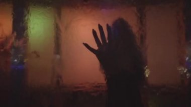 Siyah zarif elbiseli, sarı saçlı genç bir kadının silueti. Dans eden ve sanat objesinde poz veren kız Düşen suyla ve renk değiştiren ışıkla.