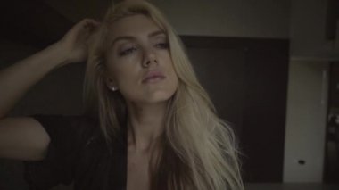 Modern dairede sarışın, uykulu genç bir kadının yüzü ve vücudu görülüyor. Siyah iç çamaşırlı düşünceli bir kız şık iç çamaşırlarıyla uyanır..