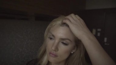 Modern dairede duran ve sarı saçları düzelten genç, şehvetli kadının yüzüne yakından bakın. Düşünceli kız şık bir iç mekanda poz veriyor..