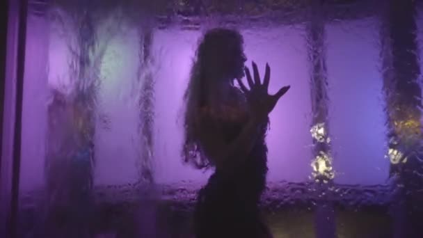 黒の小さなドレスでブロンドの髪の若い女性のシルエット 落ちる水と変化する色の光とアートオブジェクトの女の子のダンスとポーズ — ストック動画