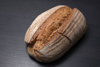 Siyah arka planda taze oval ekmek. Kesilmemiş bir somun ekmek. Lezzetli hamur işleri.