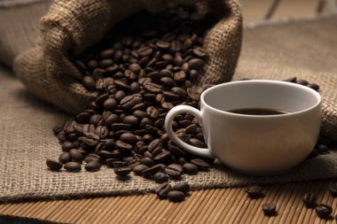 Kahve çekirdekleri torbadan döküldü. Yakınlarda bir fincan kahve var..