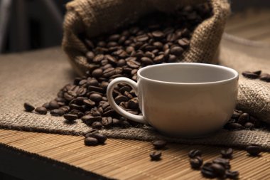 Ön planda küçük beyaz bir kahve fincanı. Kavrulmuş kahve çekirdeği.