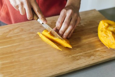 Ön taraftan görünen sağlıklı bir salata hazırlamak için tahta tahtada mango kesen bir kadın.