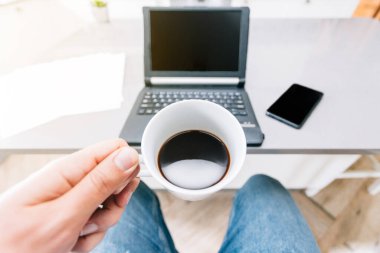 Adam tabletle, cep telefonuyla ve mutfak masasında kahve içen kağıtlarla telgraf çekiyor.