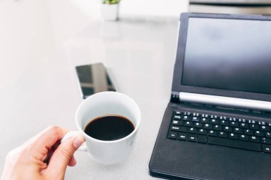 Adam tabletinden ve cep telefonundan haberleri okumaya başlamadan önce bir fincan kahve içiyor.