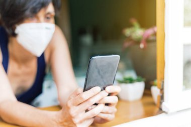 Kadın penceresinden konuşuyor ve koronavirüs karantinası sırasında maske takıyor.