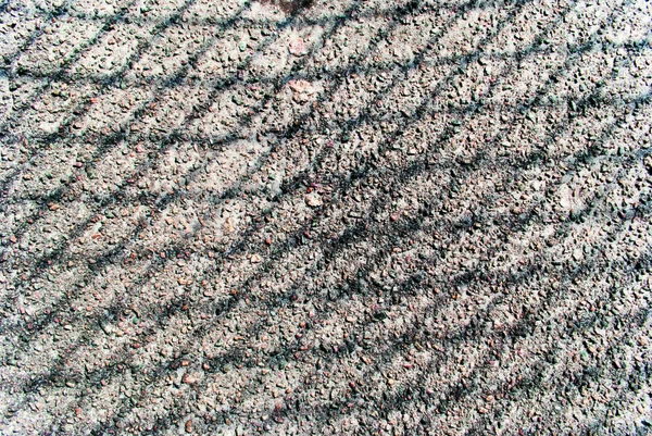 Çitlerden gelen çakıl ve gölgeli asfalt, ortadan kırılmış.