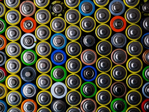 A large number of old AA batteries of different colors. Top view of alkaline batteries