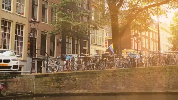 Amsterdam, Nizozemsko - září 2019: Západ slunce, vlajka komunity Lgbt visí na domě. Na mostě je mnoho kol. Amsterdam ulice krajina pohled z kanálu — Stock video