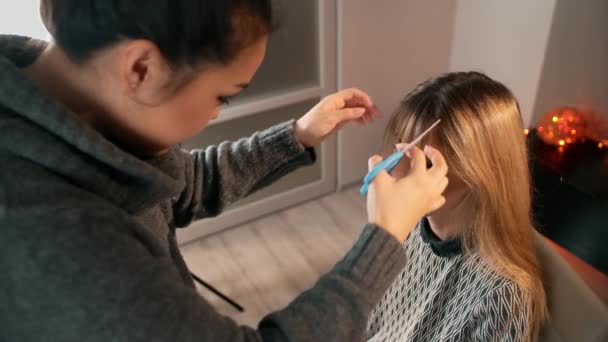 Asiatisk make-up artist klipper hårtoppar med sax. I inredningen dekorerad för firandet av jul — Stockvideo