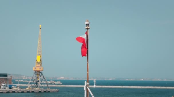 Drapeau du Canada agitant le vent. Accroché au mât d'un navire de l'OTAN amarré dans un port. Dans le contexte d'une grue pour le transbordement de marchandises — Video