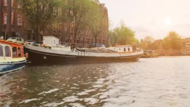Amsterdam, Hollanda - Eylül 2019: Başkentin kanallarında yüzen evler. Şehir merkezindeki evlerin cepheleri. Gün batımı. Işınlar kameraya çarptı.