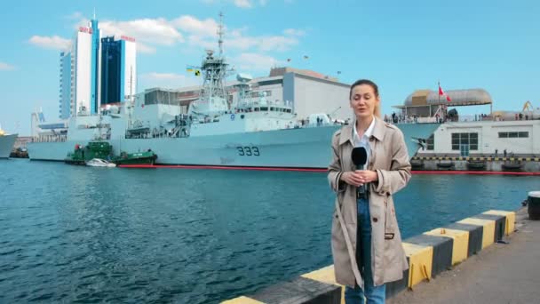 Journaliste de télévision avec un microphone fonctionne à la caméra. Dans le contexte des navires de l'OTAN amarrés dans le port. live news performance — Video