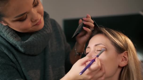 Maquillaje asiático artista hace maquillaje, con un pincel pinta las sombras sobre los ojos. En el contexto de la atmósfera navideña, de cerca — Vídeos de Stock