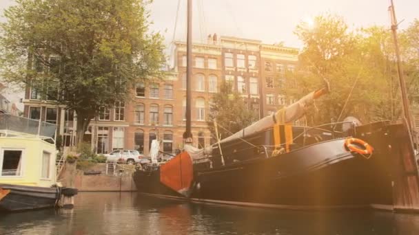 Amsterdam, Netherlands - September 2019: Lots of houseboats and ships moored in the streets. Facades of houses in the city center. The rays of sunset fall into the lens. View from the canal — Stock Video