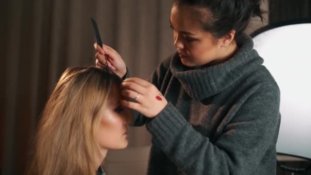 Asiatische Friseur oder Visagist kämmt den Kopf einer kaukasischen blonden Frau mit einer Haarbürste. Vorbereitung auf den Haarschnitt — Stockvideo