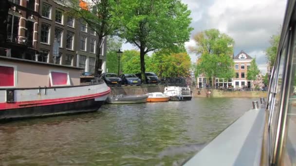 Амстердам, Нідерланди - вересень 2019: Вузька вулиця і канал у столиці. Припарковані машини стоять. Зелені дерева. Літній краєвид — стокове відео