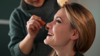 Çok ırklı genç kadın makyözleri model olarak makyaj yapıyor. Model gülümser, güler ve sevinir.