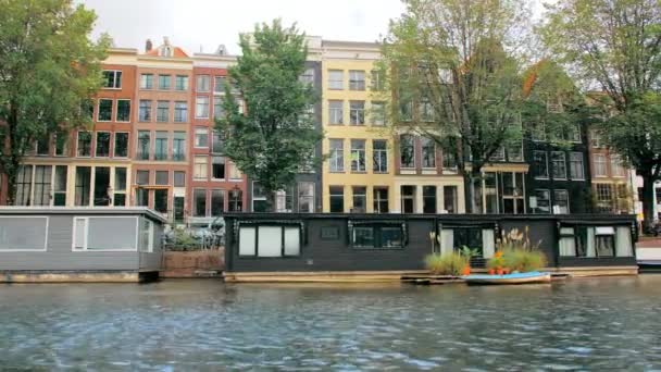 Άμστερνταμ, Ολλανδία - Σεπτέμβριος 2019: Μαύρο πλωτό σπίτι και σκάφος αγκυροβολημένο στους δρόμους. Πρόσοψη σπιτιών στο κέντρο της πόλης. Θέα από το κανάλι — Αρχείο Βίντεο