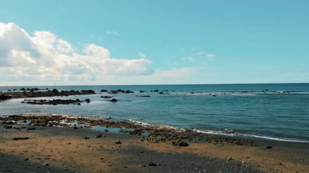 Бирюзовая вода океана. Пляж на острове с черным вулканическим песком. Белые облака висят над морем. Понятие свободы, умиротворения — стоковое видео