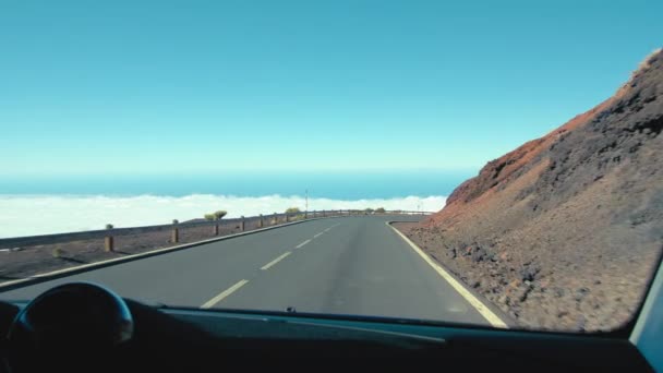 Araba asfalt yolda gidiyor. Vadinin üstünde bulut denizi ve dağlık bir tepeyi kaplayan ormanın olduğu güzel bir manzara. — Stok video