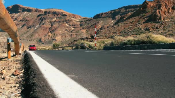 Piros ismeretlen autó lovagol végig egy hegyi aszfalt úton a sivatagban. Fényes útjelzések. A vulkáni csúcsok közepette. A tökéletes útfelület fogalma — Stock videók