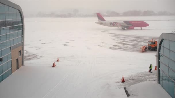 LVIV, Ucrania - enero de 2019: el avión de pasajeros rosa se está preparando para despegar, moviéndose a lo largo de la plataforma del aeródromo. Mal tiempo, no volando. fuerte tormenta de nieve y fuerte viento. trabajos de quitanieves . — Vídeo de stock