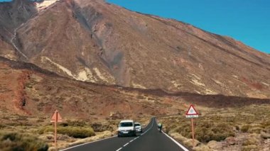 Araba asfalt yeni bir yolda ilerliyor. İçeriden. Bisikletçilerden oluşan bir ekip yolda buluşur. Çölün dışında volkanik bir adada. Dağ zirvesi ve kaya tepeleri. Uzun yolculuklar ve seyahatler