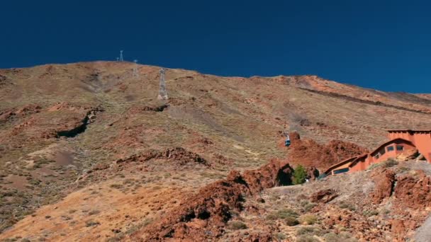 Cabina del teleférico se mueve a lo largo del teleférico. En el fondo de una alta montaña, un pico de un volcán — Vídeo de stock