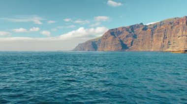 Arka planda dev bir kaya var. Sarı kayalar kaynayan turkuaz sörf. Kör edici gün ortası güneşi lav kayalık sahilini aydınlatıyor. Aktif, ekolojik ve fotoğraf turizmi kavramı