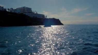 Tepedeki bir otel kompleksinin silüeti. Okyanus suyunda güneşli, güzel bir yürüyüş yolu. Sakin bir dinlenme konsepti.