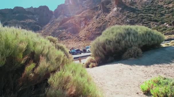 Ilha para descanso e carros de lodo em uma estrada de asfalto de montanha no deserto. Contra o fundo de um pico de um vulcão. Marcas brilhantes na estrada. Os raios de sóis caem na moldura — Vídeo de Stock