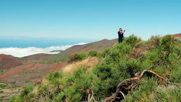 Mujer rubia atractiva hace selfie usando un teléfono inteligente. Hermoso paisaje con mar de nubes sobre el valle y bosque que cubre la cresta de la montaña. concepto de inspiración, libertad — Vídeos de Stock