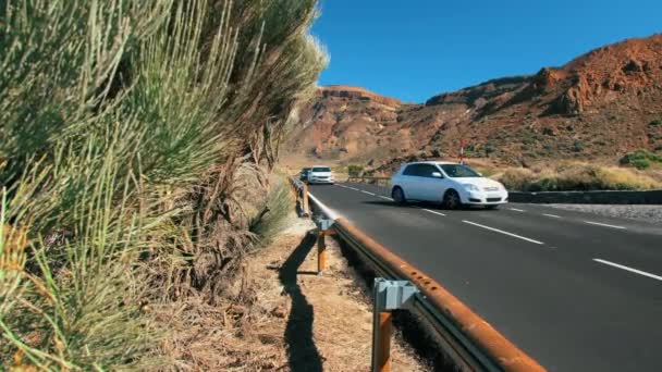 Auto non riconosciute stanno guidando lungo una strada asfaltata di montagna nel deserto. Luminose indicazioni stradali. Sullo sfondo di cime vulcaniche. Il concetto di superficie stradale perfetta — Video Stock