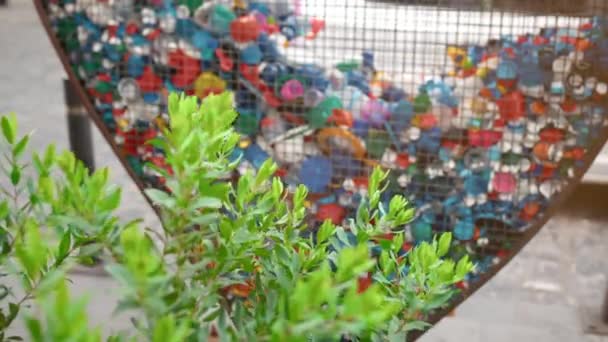 Concept van het inzamelen van plastic afval en afval in steden. Groene plantenstruik en hartvormige ijzeren kooi voor het verzamelen van pet covers en flessen. Begrip natuurbehoud, milieuverontreiniging — Stockvideo