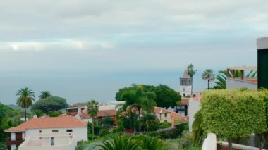 Cennetteki evler. Tropik manzara, sık bitki örtüsü ve deniz kenarında palmiye ağaçları olan dağ vadisi. Arka planda küçük bir dağ kasabası. Kanarya Adalarının egzotik manzarası