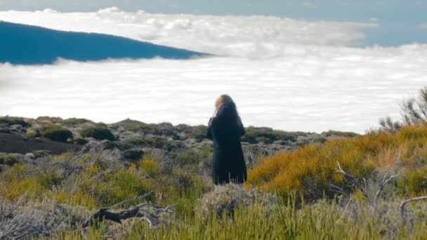 Donna attraente è in piedi sul bordo di una scogliera. Bellissimo paesaggio con mare di nuvole sopra valle e foresta che copre cresta di montagna. concetto di ispirazione, libertà — Video Stock