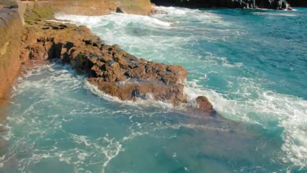 海のターコイズブルーの波が海岸の黄色の石に打ち勝ちます。巨大な白い泡とスプレーフォーム。海の中のエブスの概念は — ストック動画