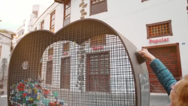 Canarische Eilanden, Spanje - januari 2019: Vrouw gooit plastic kapjes in een ijzeren kooi in de vorm van een hart om plastic te verzamelen. Begrip inzameling van kunststofafval, natuurbehoud. — Stockvideo
