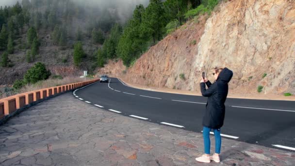 A női blogger videótartalmakat lő le egy mobiltelefonra. Vastag köd száll le egy fenyőerdőre a háttérben lévő hegyekben. Koncepcióbefolyásoló tartalmat készít a társadalmi — Stock videók