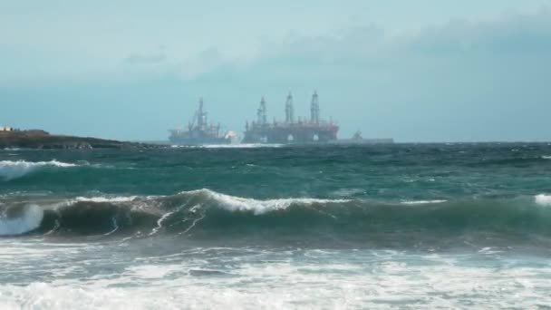 Buque cisterna cerca de plataformas petrolíferas en el océano frente a la costa. Mar tormentoso, olas y espuma. Concepto de extracción de petróleo de la plataforma oceánica y medio ambiente contaminante — Vídeo de stock