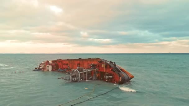 Φορτηγό πλοίο, βυτιοφόρο προσάραξε και κύλησε στη θάλασσα με κύματα συννεφιασμένων καιρικών συνθηκών. ανθρωπογενής καταστροφή, ρύπανση του θαλάσσιου οικοσυστήματος από εκπομπές από το σκάφος. το ηλιοβασίλεμα ή την ανατολή. κεραία — Αρχείο Βίντεο